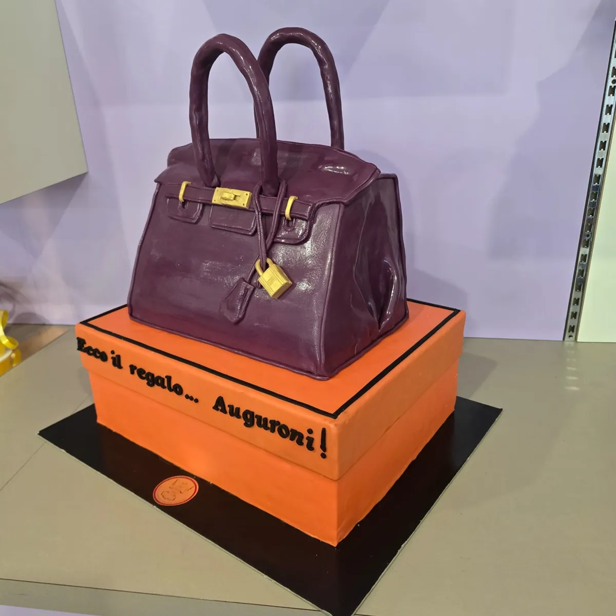 Fashion cake: borsa viola in pasta di zucchero su scatola arancione con scritta Auguroni